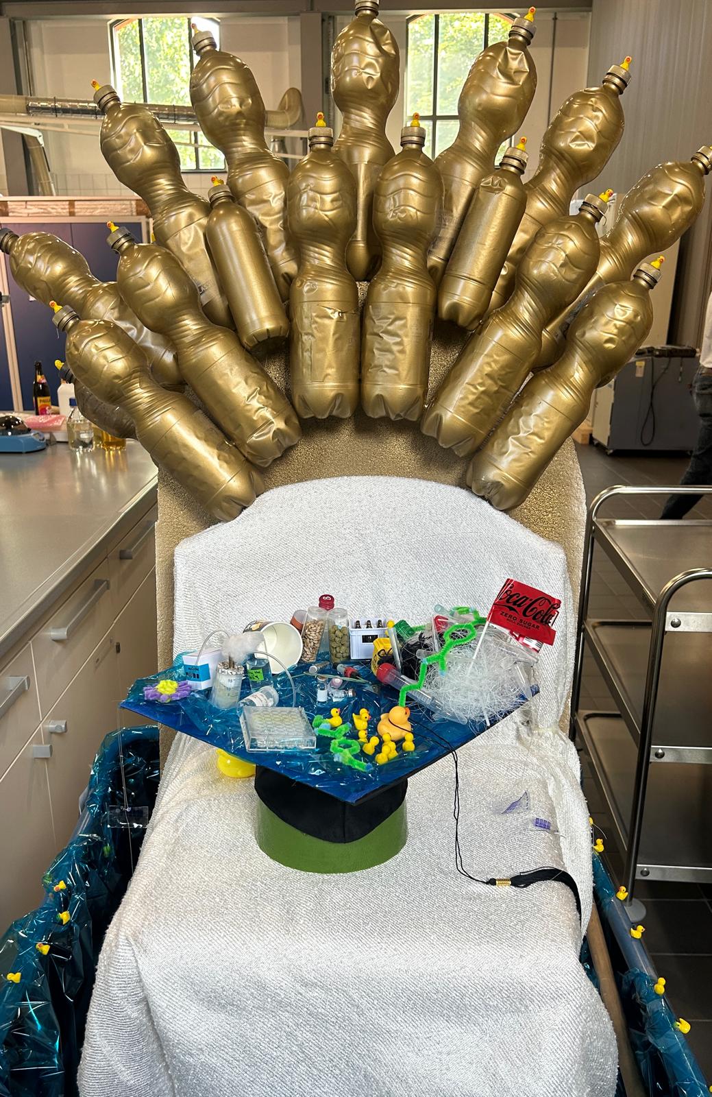 Doktorwagen - ein auf dem Ziehwagen befestigter Sitzt mit Rücklehne auds goldenen PET-Flaschen und dem Doktorhut auf dem Sitzt